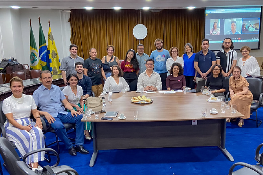 Grupo de pessoas das comissões organizador e eleitoral da Constituinte sentadas ou em pé ao redor de uma grande mesa na sala dos Conselhos da UFC