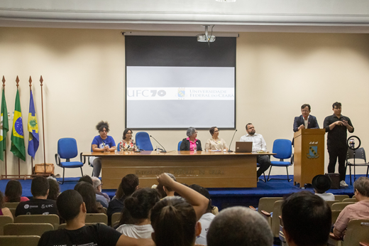 Imagem: No Auditório da Reitoria, o reitor Custódio Almeida discursa no púlpito para a plateia do evento Estatuinte em Debate; na mesa, estão Dandhara Cavalcante (estudante de História), Profª Diana Azevedo (vice-reitora), Elaine Teixeira (TAE) e Daniel Fonsêca (coord. de Articulação Política do Gabinete da Reitoria).